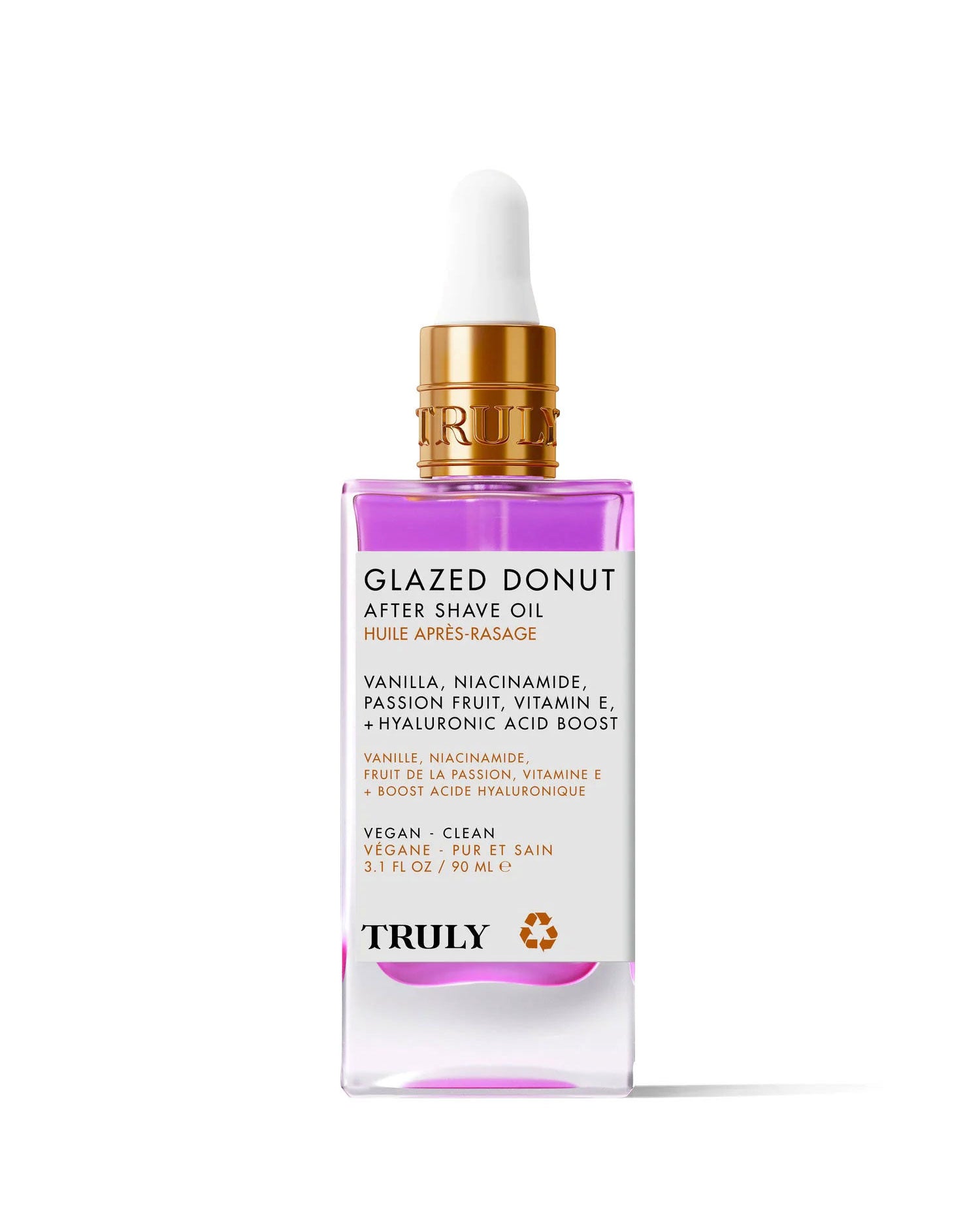 A pink and clear glass dropper bottle labeled Glazed Donut After Shave Oil, highlighting skin-smoothing niacinamide, vitamin E, and hyaluronic acid, is shown on a light pink background.
