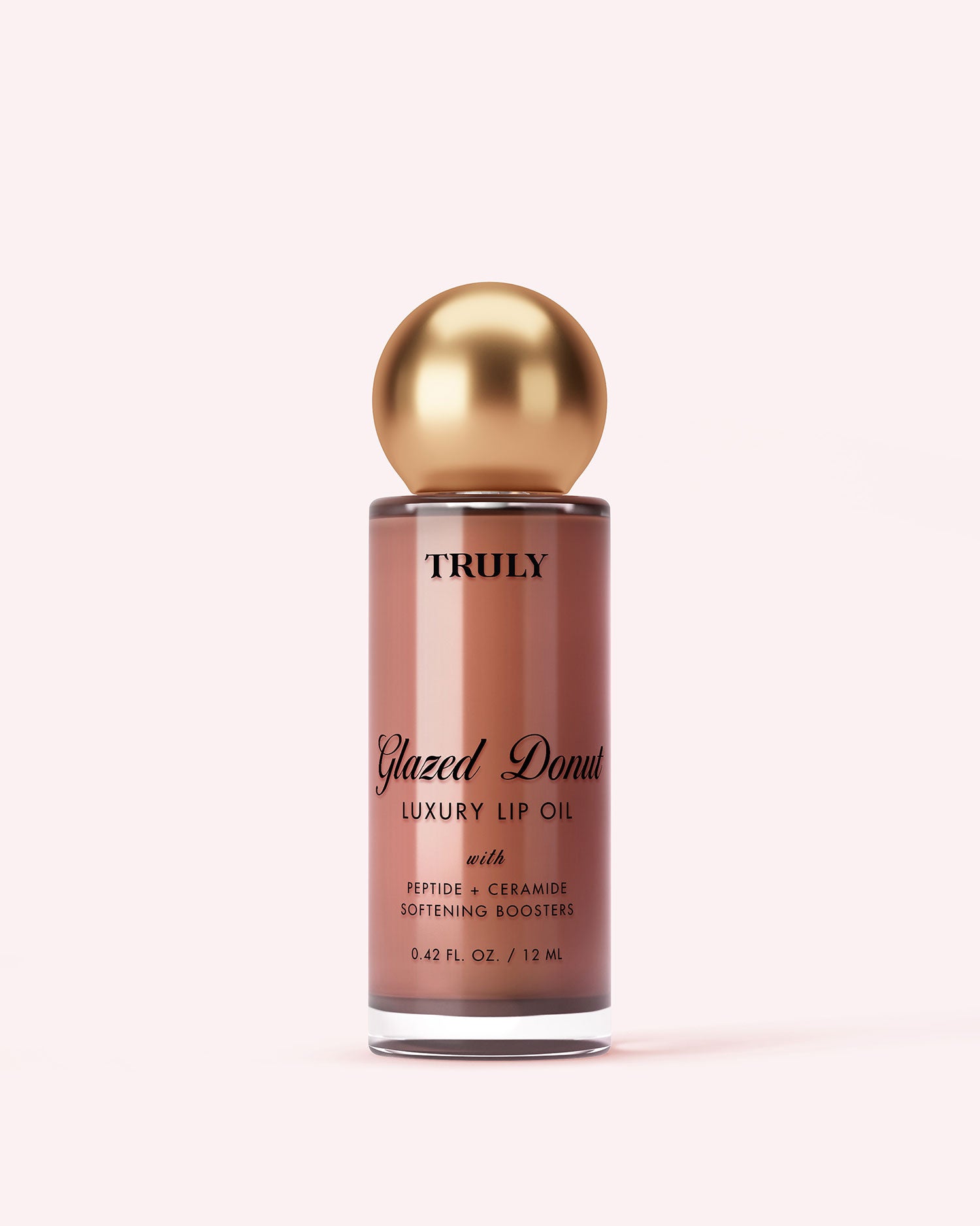 A bottle labeled Truly Beauty The Glossy Duo, featuring a gold spherical cap and filled with pinkish-brown liquid, is displayed against a pale pink background.