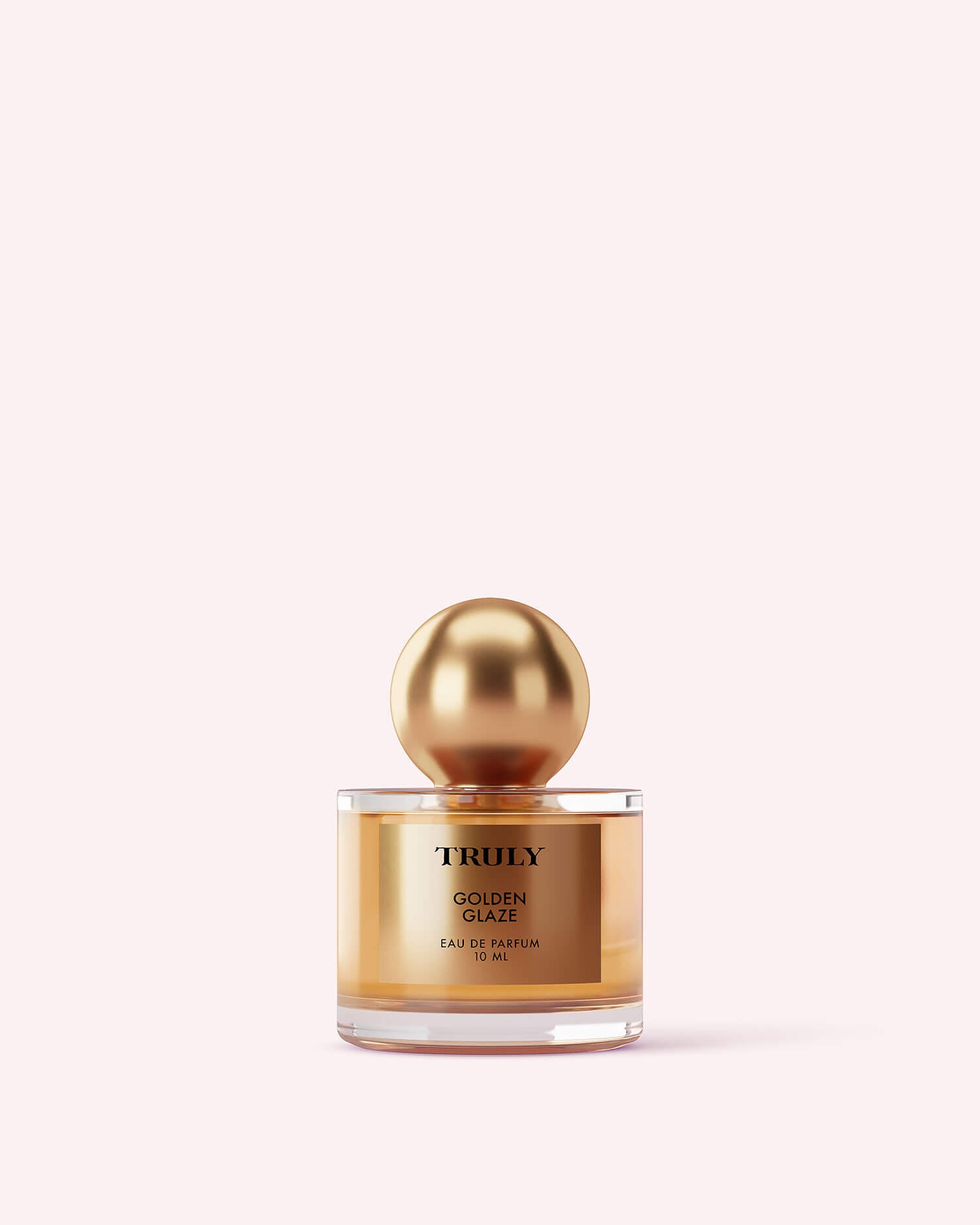 A gold and clear bottle from Truly Beautys The Perfumers Set, with a shiny gold spherical cap, stands against a pale pink background, evoking the luxurious scents within.