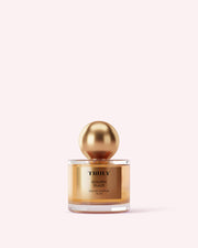 A gold and clear bottle from Truly Beautys The Perfumers Set, with a shiny gold spherical cap, stands against a pale pink background, evoking the luxurious scents within.