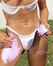 A woman in a white bikini applies Truly Beauty’s Smooth Legend Shave Routine, a hand-whipped swirl enriched with coconut and vitamin E, to her upper thigh and bikini line to soften and exfoliate skin.