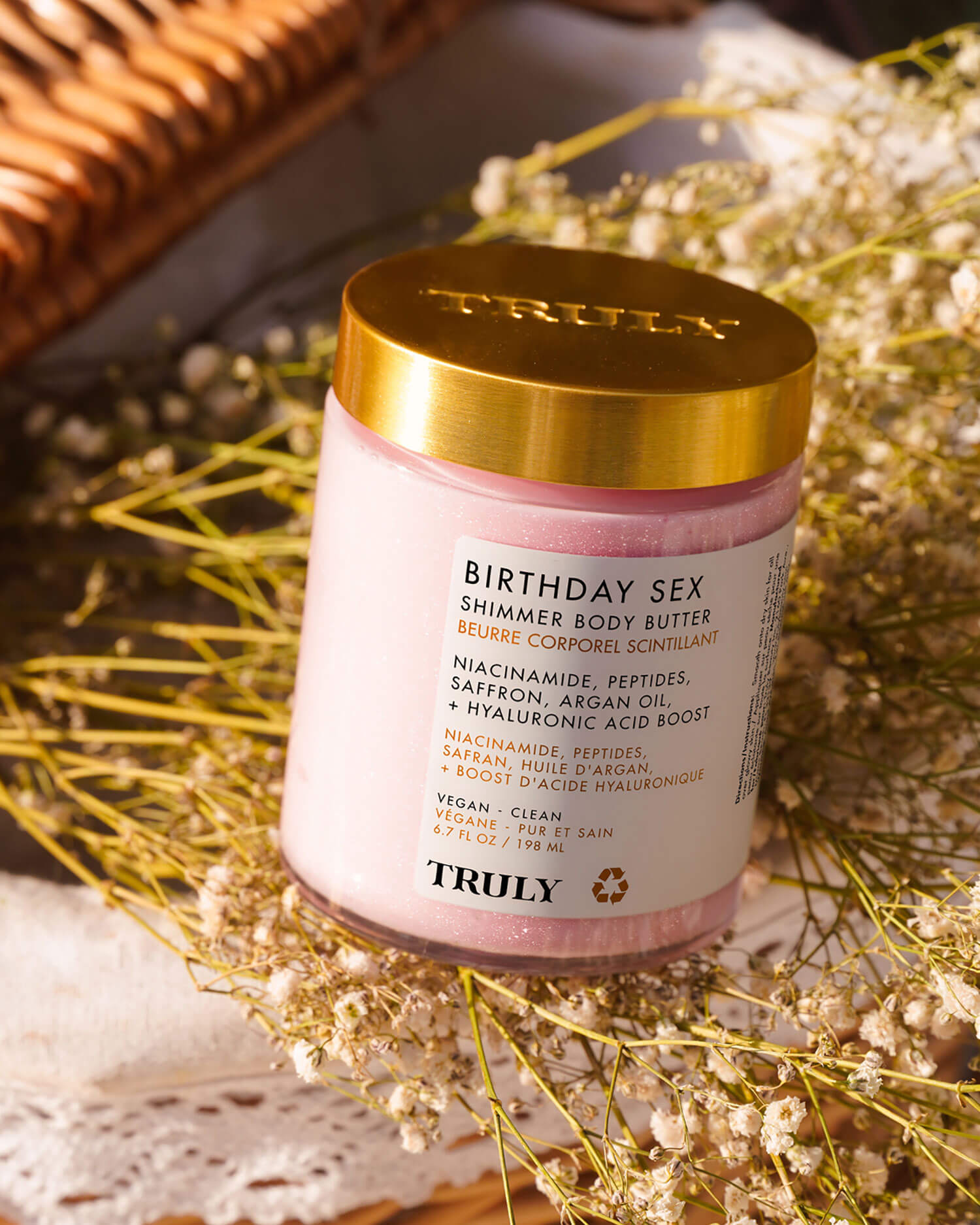 A jar from Truly Beautys Birthday Sex Luxury Trio with a gold lid rests on white lace, surrounded by dried flowers and warm light. Its label highlights jasmine and saffron—perfect for your scent-layering ritual.