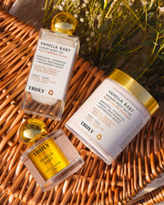 The Vanilla Baby Luxury Trio by Truly Beauty—featuring body oil, body butter, and perfume—rests on a woven surface with sunlight and greenery, inviting you to enjoy warm vanilla aromas for radiant skin.