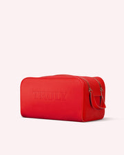 The Candy Apple Vanity Case by Truly Beauty is a bright red rectangular vegan leather bag with a handle and zipper, TRULY embossed on the front. Perfect as a skincare travel pouch, it’s shown on a plain light background.