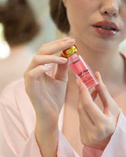 A person in a pink robe holds The Glossy Duo by Truly Beauty, focusing on their hands and lips as if about to apply the products for smooth, nourished lips and hydrated skin.