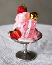 The Glossy Duo by Truly Beauty sits beside melting pink ice cream and fresh strawberries in a glass dish, all arranged on a white textured surface.