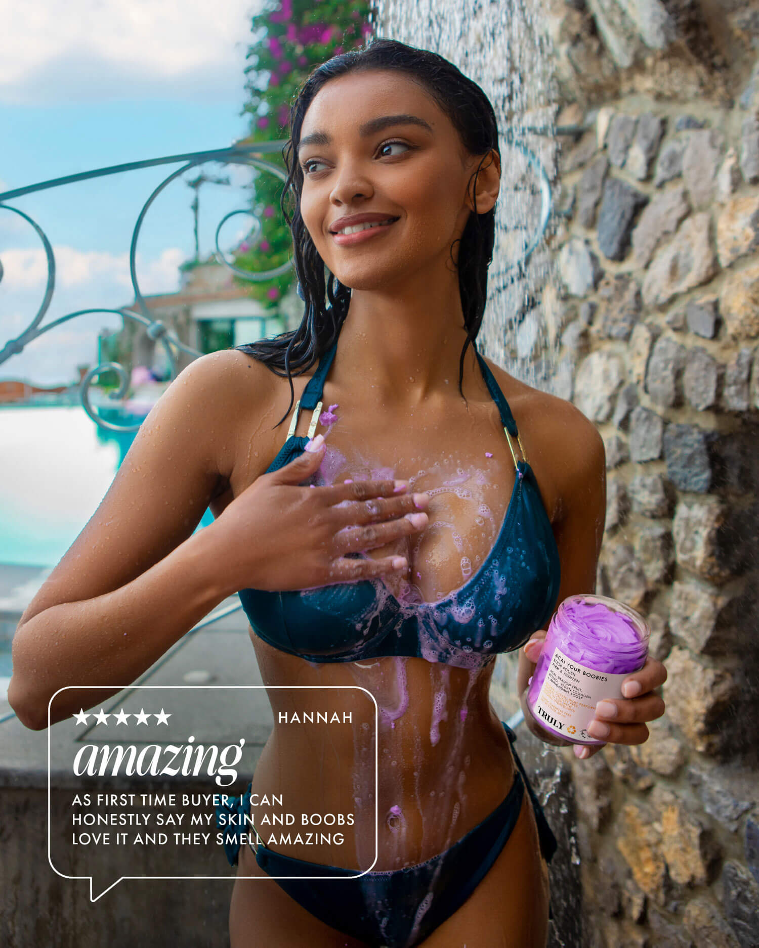 A smiling woman in a black bikini applies Truly Beauty’s For Your Boobs Routine purple firming body scrub to her chest by a stone wall and pool, holding the jar. A text overlay displays a positive customer review.