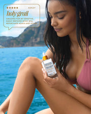 A woman in a pink bikini sits by the water, smiling and holding Truly Beauty’s Coco Cloud After Shave Serum. Text reads: Holy grail—amazing for my sensitive, easily irritated skin! Will repurchase again and again.
