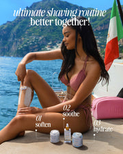 A woman in a pink bikini shaves her leg on a dock by the water, mountains and an Italian flag behind her. In front, Truly Beauty’s Coco Cloud After Shave Serum promises smooth, soft skin with hydrating argan oil and unique hydration benefits.