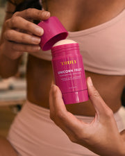 A person in a beige bikini opens a pink stick of Truly Beauty’s The Viral Edit deodorant, holding it close to their body and lifting the lid with the other hand.