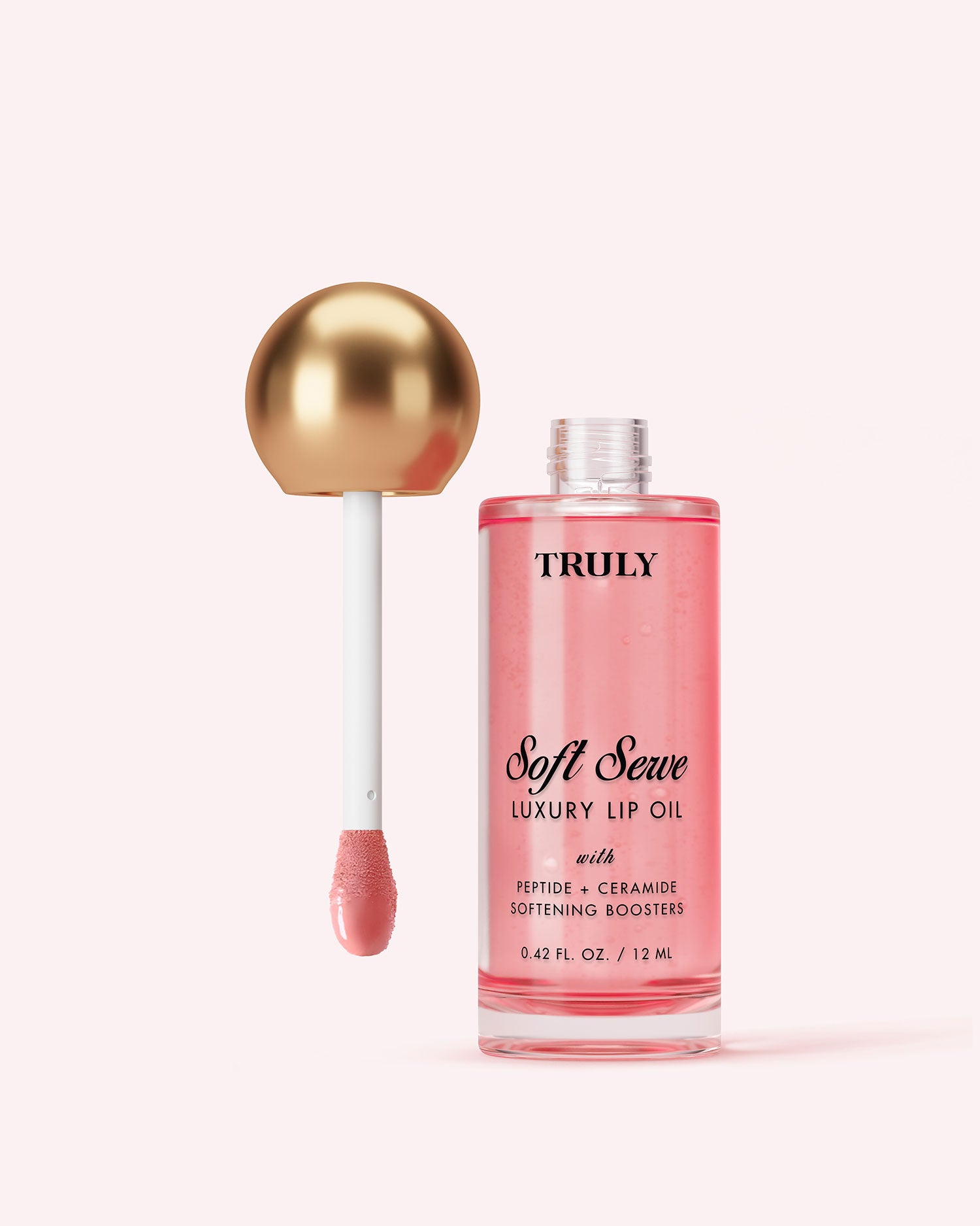 A bottle of Truly Beauty Luxury Peptide Lip Oil with pink liquid and a gold-capped applicator wand dipped in the oil, set against a light pink background.