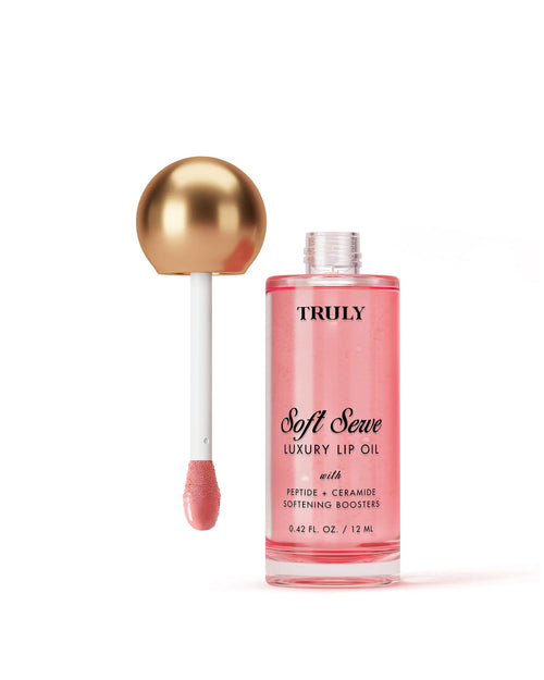 A bottle of Truly Beauty Luxury Peptide Lip Oil with a gold-topped applicator wand, filled with pink liquid, displayed against a light white background.
