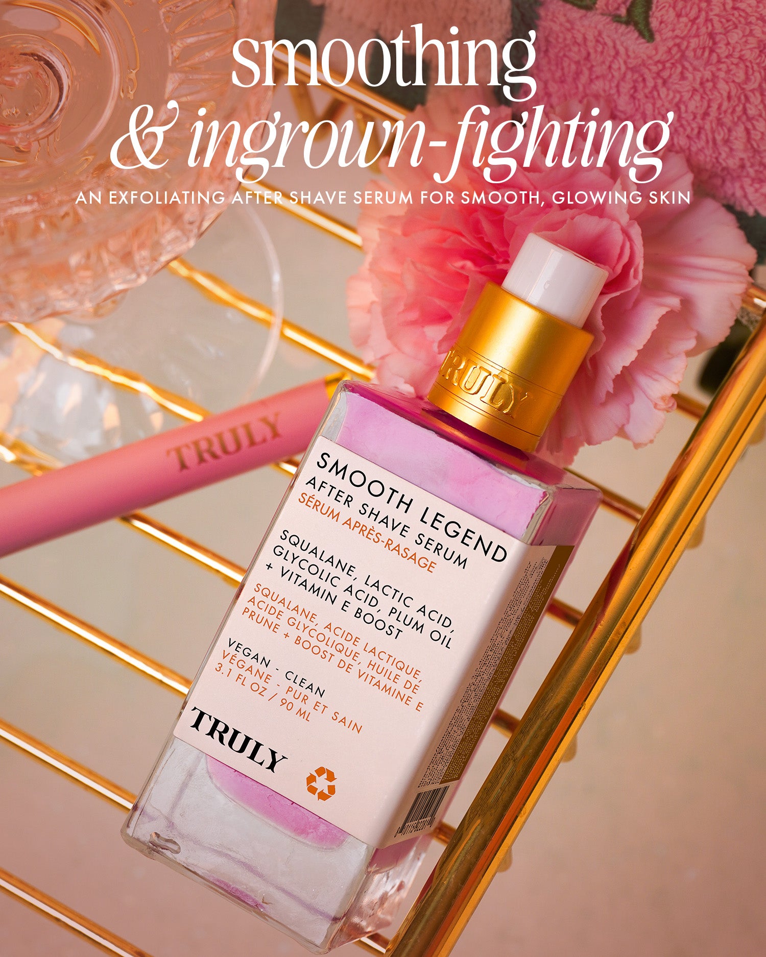 A bottle of Truly Beauty Smooth Legend After Shave Serum with exfoliating AHAs and a pink-and-gold dropper rests on a pink surface, surrounded by a flower, pink razor, and decorative text highlighting its skin-smoothing benefits.