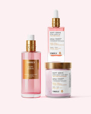 Three pink products from Truly Beauty’s Soft Serve Luxury Trio—spray bottle, dropper bottle, and “Soft Serve” jar—are displayed against a light background, offering strawberry-scented hydration with peptides and strawberry extract.
