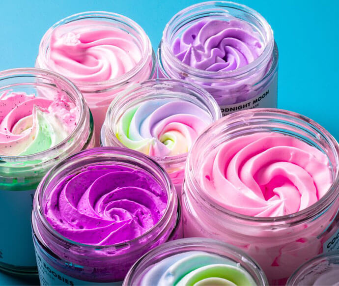 Six Truly products from the Truly Mystery Box Of 6 Products are arranged on a bright blue background, styled with decorative swirled tops in pastel shades of pink, purple, mint green, and rainbow swirl.