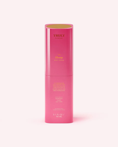 A tall, cylindrical pink bottle of Truly Beauty The Clearing Body Serum (3.1 fl oz/90 mL), designed to target large pores and body acne, features gold and yellow text and is displayed against a pale pink background.