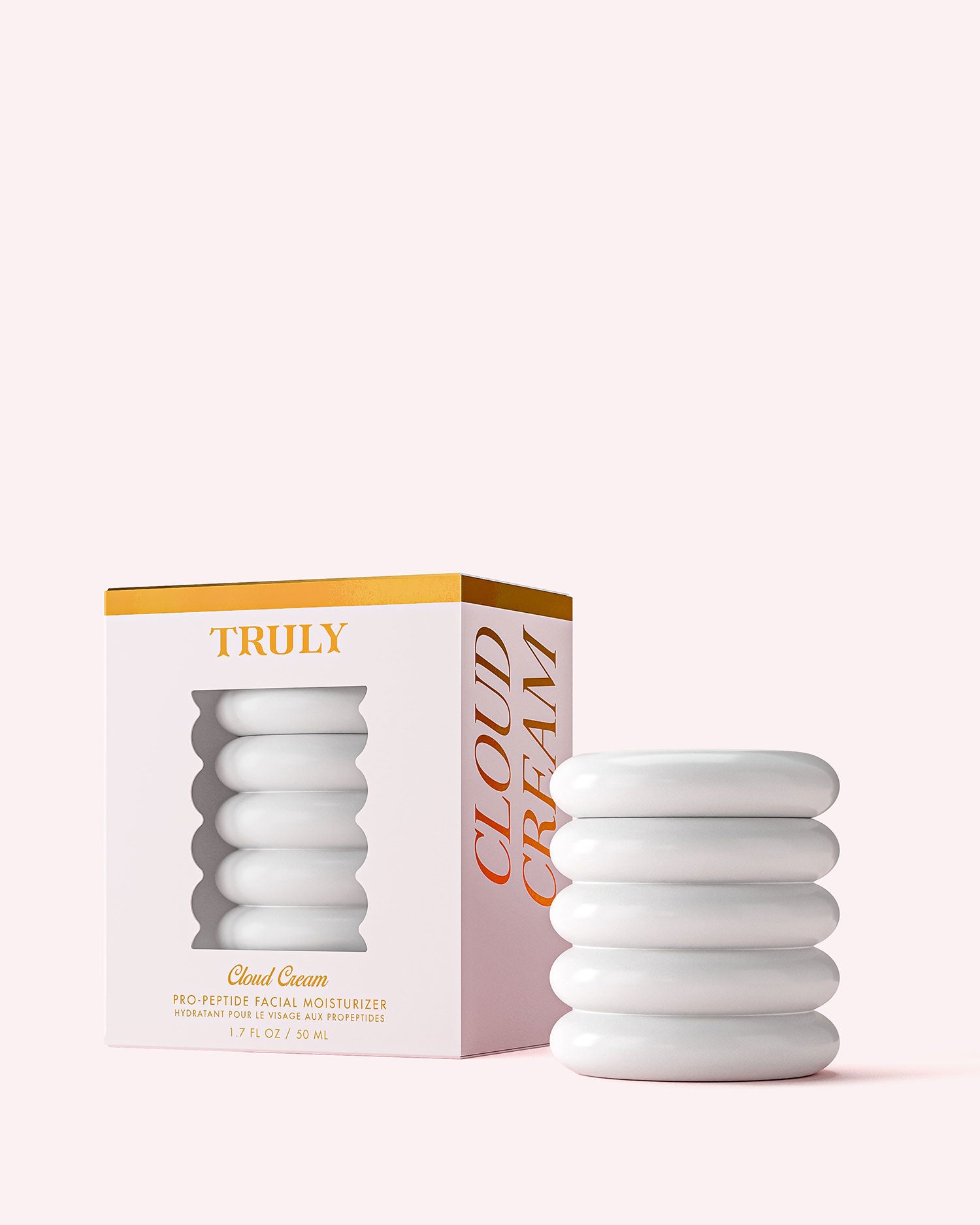 A white, ribbed jar of Truly Beauty’s Cloud Cream Pro-Peptide Facial Moisturizer sits beside its white, gold-accented box with a cutout displaying the jar. Both are set against a pale pink background.