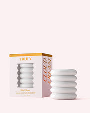 A white, ribbed jar of Truly Beauty’s Cloud Cream Pro-Peptide Facial Moisturizer sits beside its white, gold-accented box with a cutout displaying the jar. Both are set against a pale pink background.