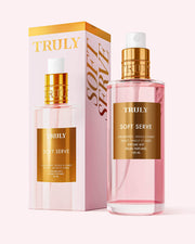 A pink bottle of Truly Beauty Soft Serve Perfume Mist with a gold cap sits beside its matching box, both adorned with gold lettering and soft pink accents, showcasing its strawberries and cream scent.