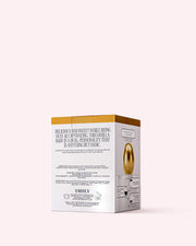 A rectangular white and gold Vanilla Baby Eau De Parfum box by Truly Beauty, featuring gold egg art and printed text, sits against a pale pink backdrop—ideal for fans of the scent or those loving an amber touch.