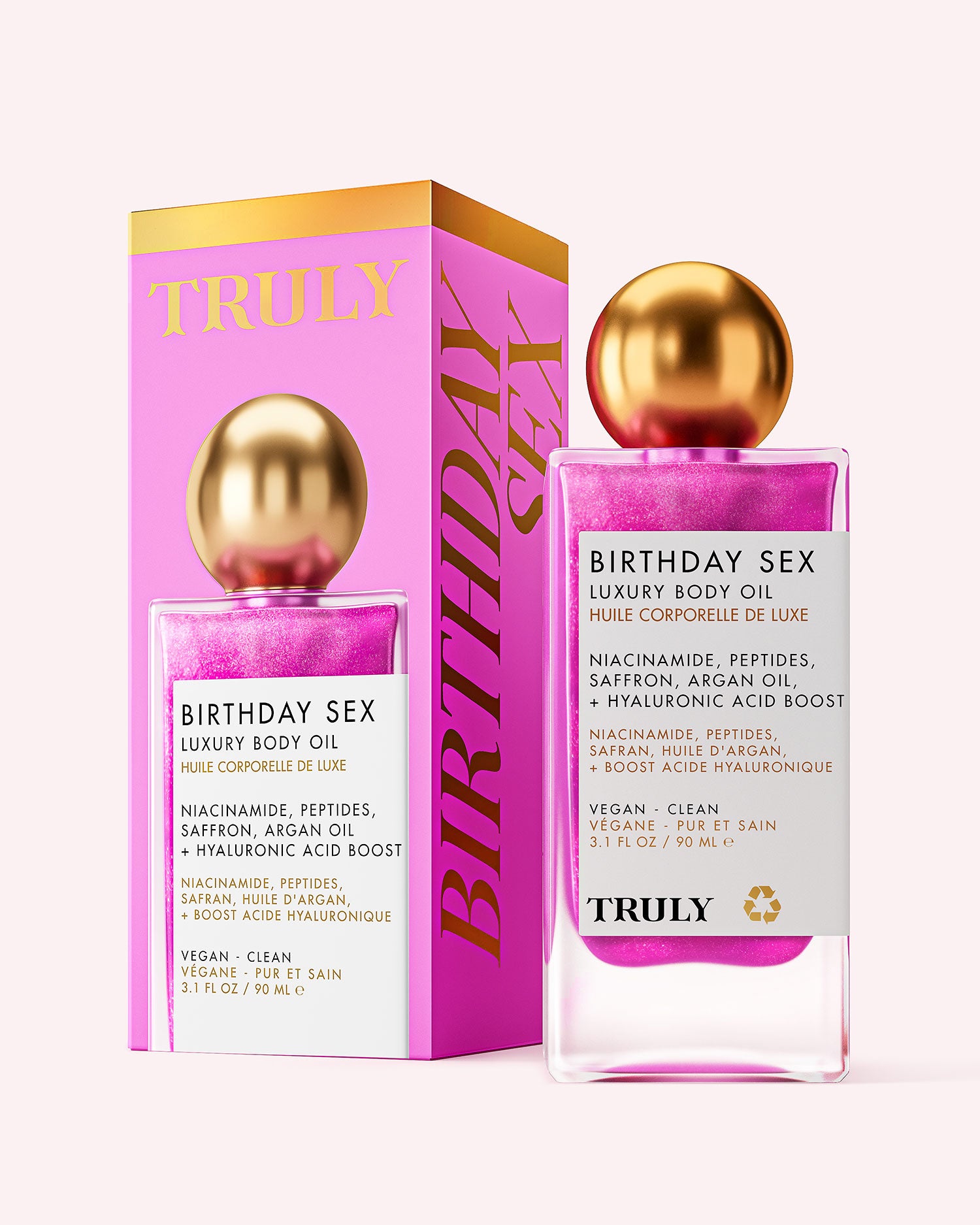 A pink and gold bottle of Truly Beauty Birthday Sex Luxury Body Oil stands before its matching box, both displaying product details and ingredients like hyaluronic acid and peptides.