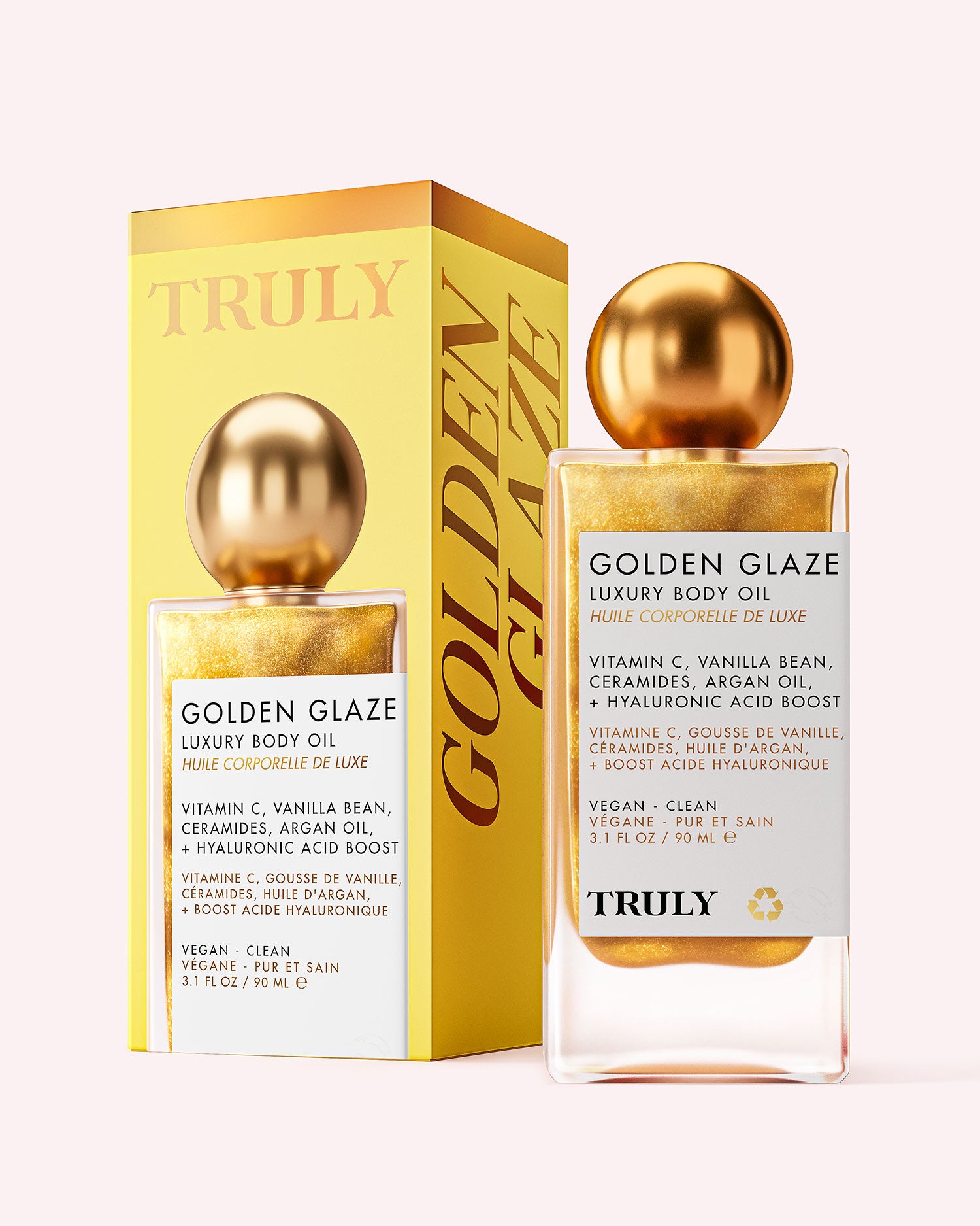 A bottle of Truly Beauty Golden Glaze Luxury Body Oil with a gold cap is placed beside its matching yellow and gold box. Both display product info and branding in black text. The oil has a shimmering gold hue and is infused with hydrating Vitamin C.