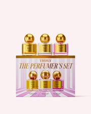 Three gold-capped perfume bottles—Golden Glaze, Vanilla Baby, and Unicorn Fruit—are displayed above a pink and gold box labeled The Perfumers Set by Truly Beauty, creating the ultimate discovery set of intoxicating fragrances.