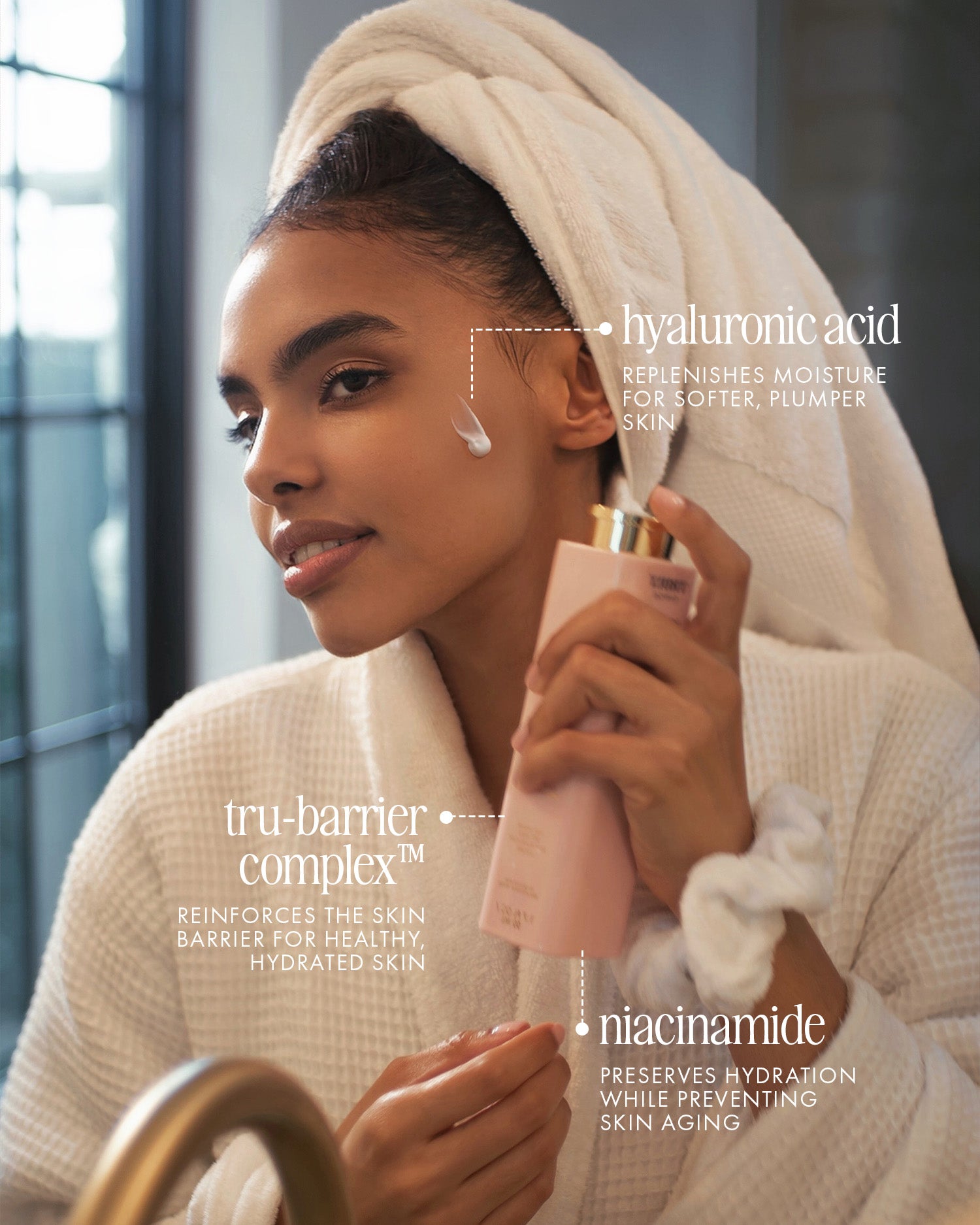 A woman in a white bathrobe applies The Face Serum Duo by Truly Beauty, featuring hyaluronic acid for moisture, tru-barrier complex for skin barrier support, and niacinamide for hydration and anti-aging.