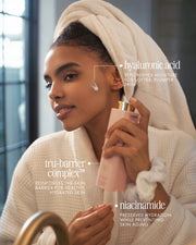 A woman in a white bathrobe applies The Face Serum Duo by Truly Beauty, featuring hyaluronic acid for moisture, tru-barrier complex for skin barrier support, and niacinamide for hydration and anti-aging.