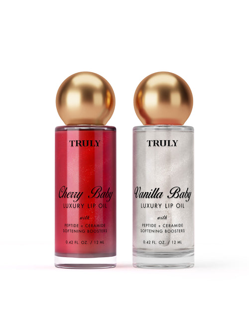 Two Truly Beauty Shimmer Duo lip oils with gold caps—Cherry Baby (red) and Vanilla Baby (white)—each deliver hydrating, glossy care in 0.42 fl oz (12 ml) bottles for nourished lips.