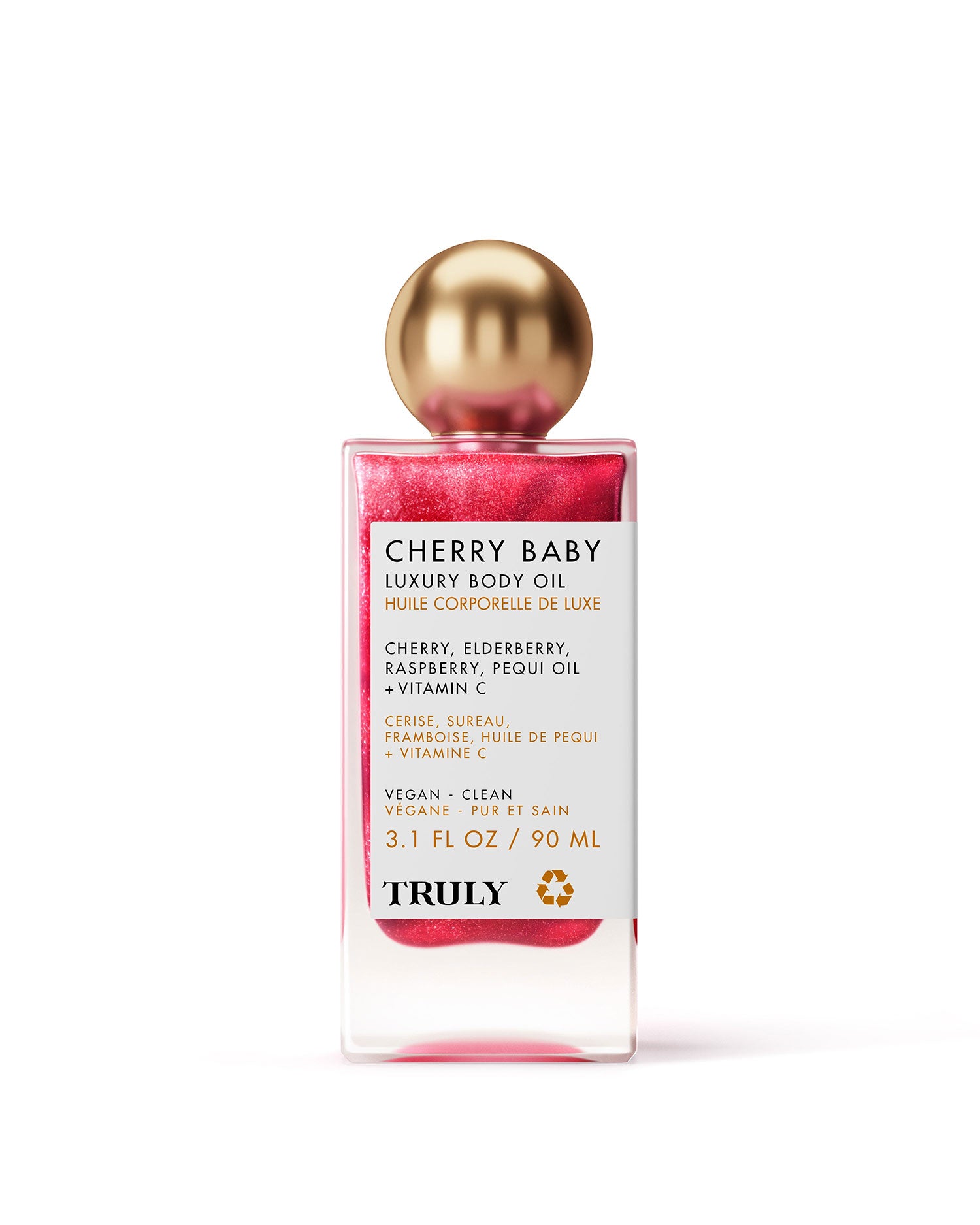 A rectangular Truly Beauty Cherry Baby Luxury Body Oil bottle with a shiny gold cap, pink shimmery oil, and a white label listing ingredients and benefits in English and French. Set against a light pink background to show its radiant shimmer.