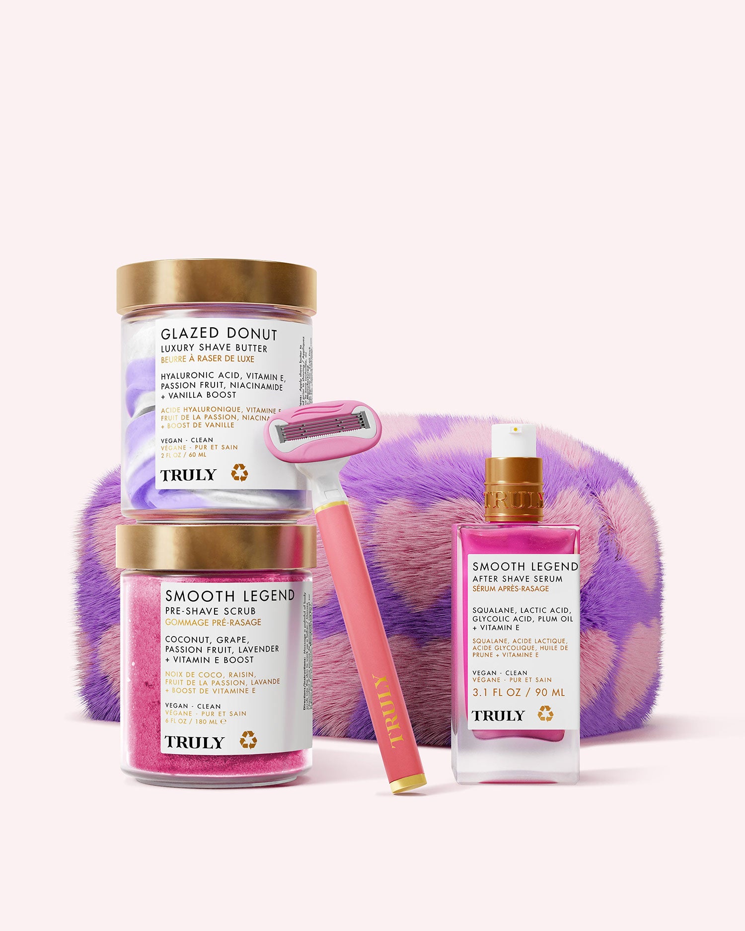 The Truly Beauty Ultimate Smooth Legend Shave Set includes Glazed Donut and Smooth Legend skincare, two jars, a bottle, a razor, and a purple-and-pink fuzzy case—all arranged on a light pink background.