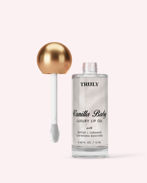 Clear bottle labeled “Truly Beauty Luxury Peptide Lip Oil” with a metallic gold and white applicator wand beside it, set against a light pink background—ideal for those seeking nourishing, hydrating lip care.