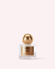 A clear glass perfume bottle with a gold cap and TRULY VANILLA BABY label stands on a pale pink background—an ideal addition to The Perfumers Set by Truly Beauty for discovering new fragrances.