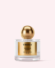 Truly Beauty’s Vanilla Baby Eau De Parfum, 50 ml, features a gold label and large gold cap, shown on a pale pink background—infused with warm amber notes for a gentle sweetness.