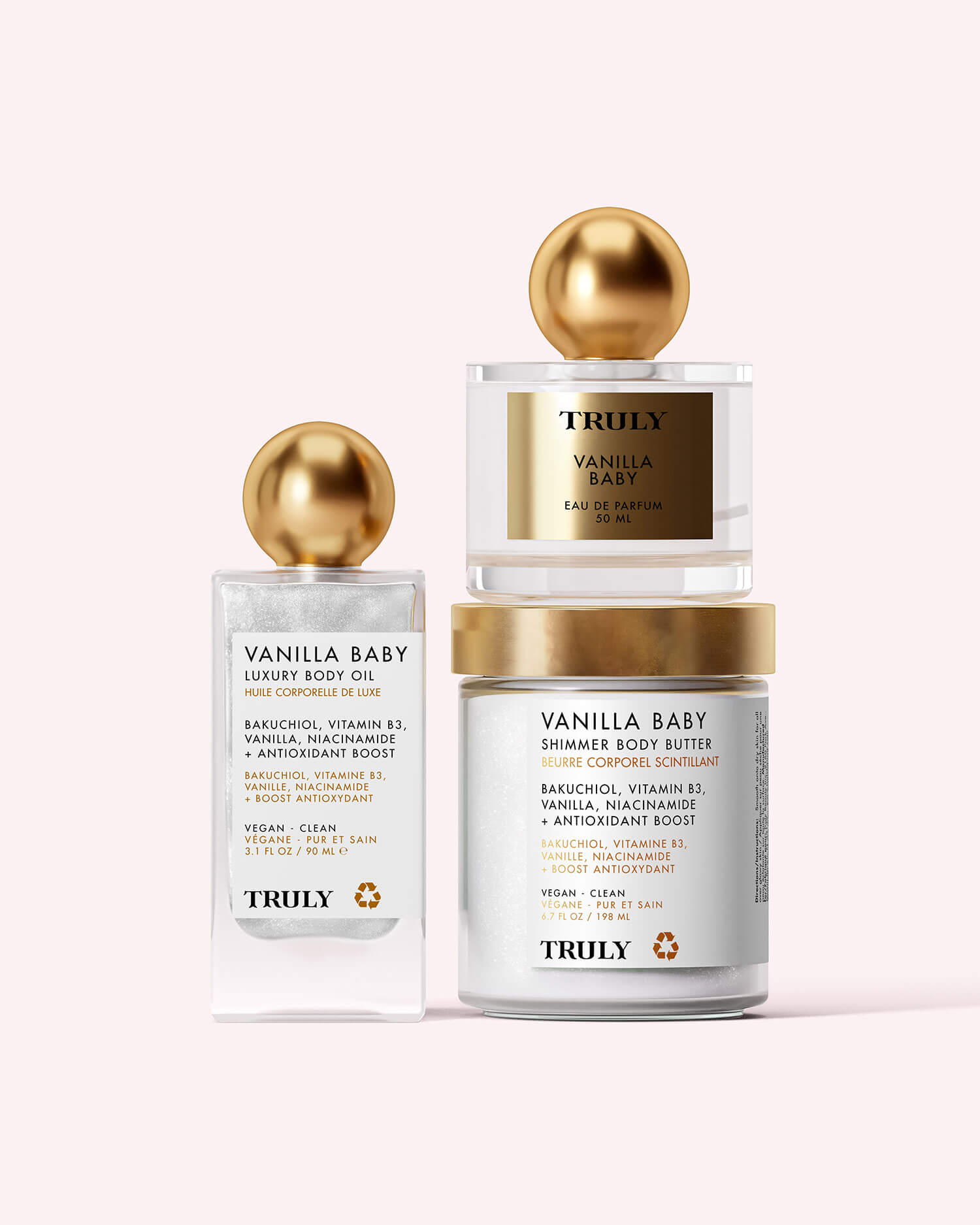 A clear glass bottle of Truly Beauty Vanilla Baby Luxury Body Oil with a gold round cap and white label listing tightening, anti-aging ingredients like bakuchiol, vitamin B3, and niacinamide, set against a light pink background.