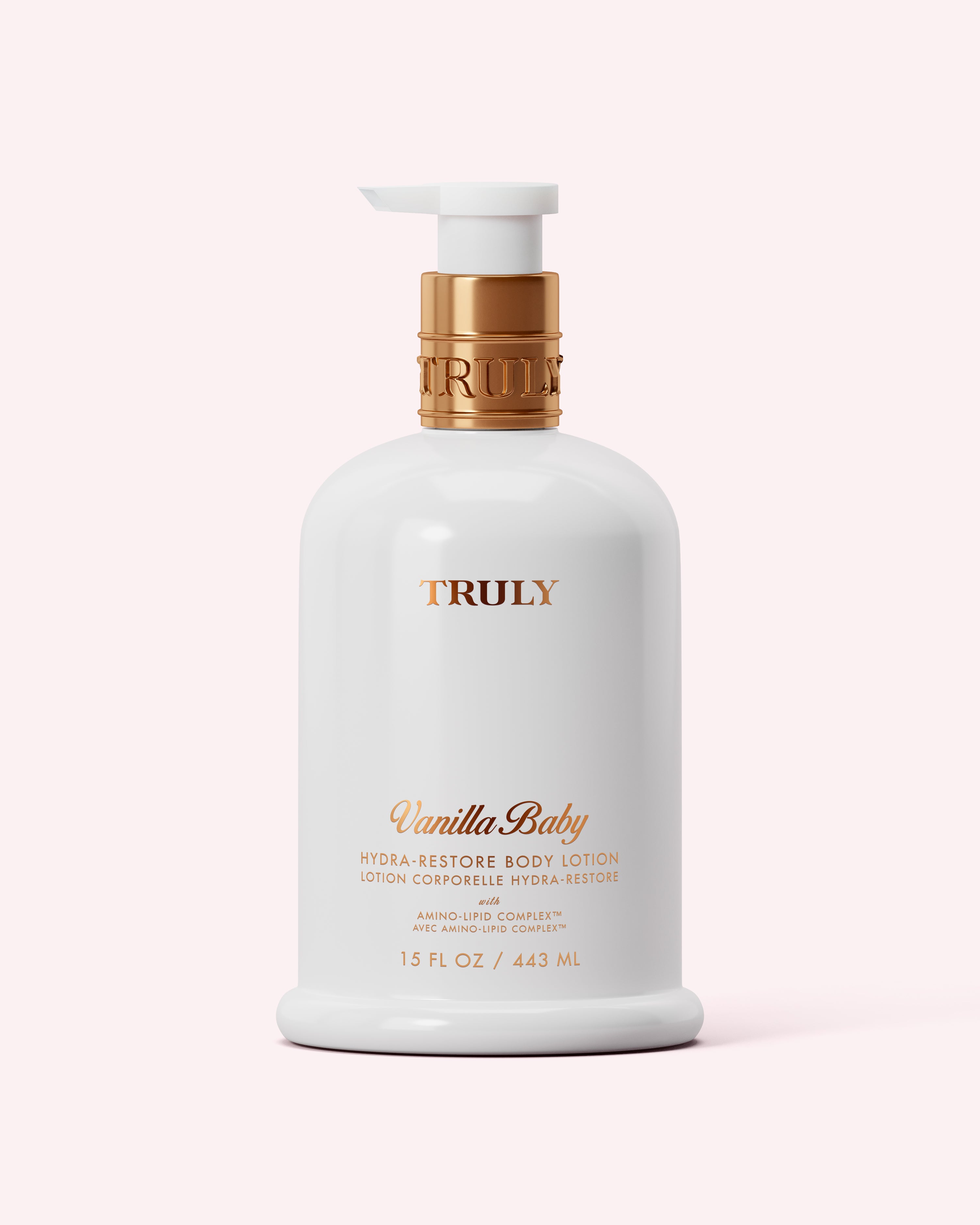 A white 15 fl oz (443 ml) bottle of Truly Beauty Hydra-Restore Body Lotion with gold pump and lettering, featuring an Amino-Lipid Complex for lasting hydration, shown against a pale pink background.