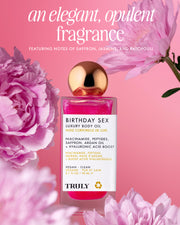 A pink bottle of Truly Beauty’s Birthday Sex Luxury Trio with a gold cap sits among pink flowers on a pink background, highlighting its elegant fragrance of jasmine, saffron, and patchouli.