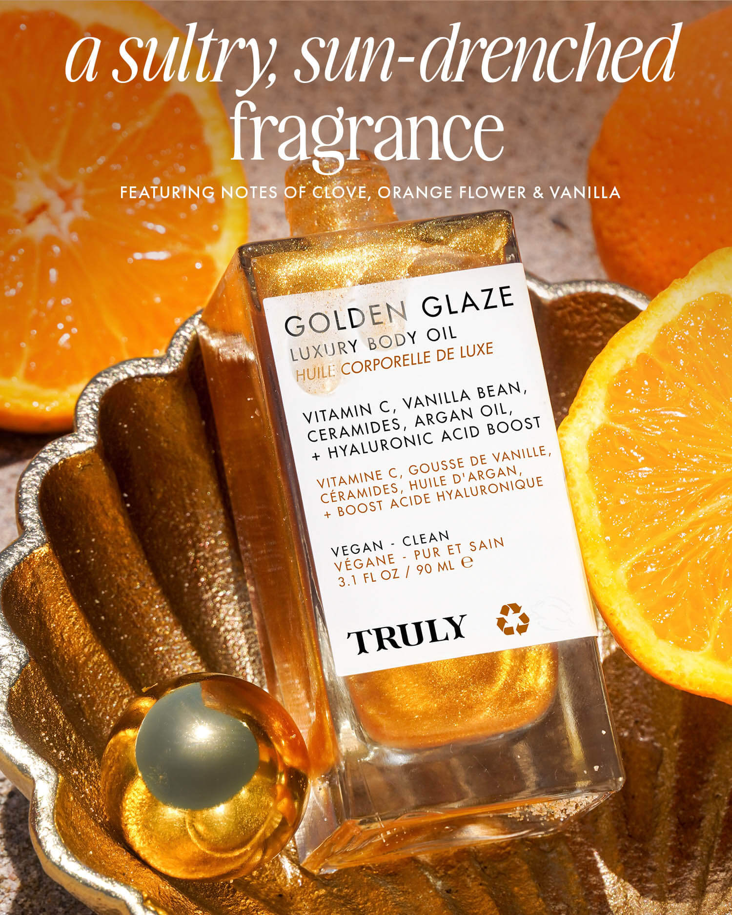 A bottle of Truly Beauty Golden Glaze Luxury Body Oil sits in a golden dish among orange slices and a gold sphere, sunlight highlighting its hydrating benefits and Vitamin C-infused fragrance.