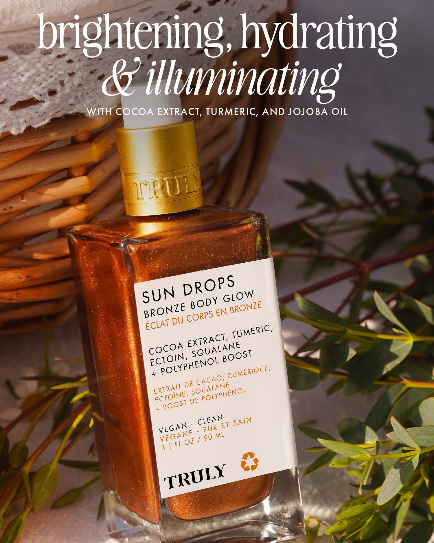 A bottle of Truly Beauty Sun Drops Bronze Body Glow with a golden cap rests on a woven basket among greenery. The label features cocoa extract, turmeric, and jojoba oil for hydrating and illuminating a sunkissed glow.