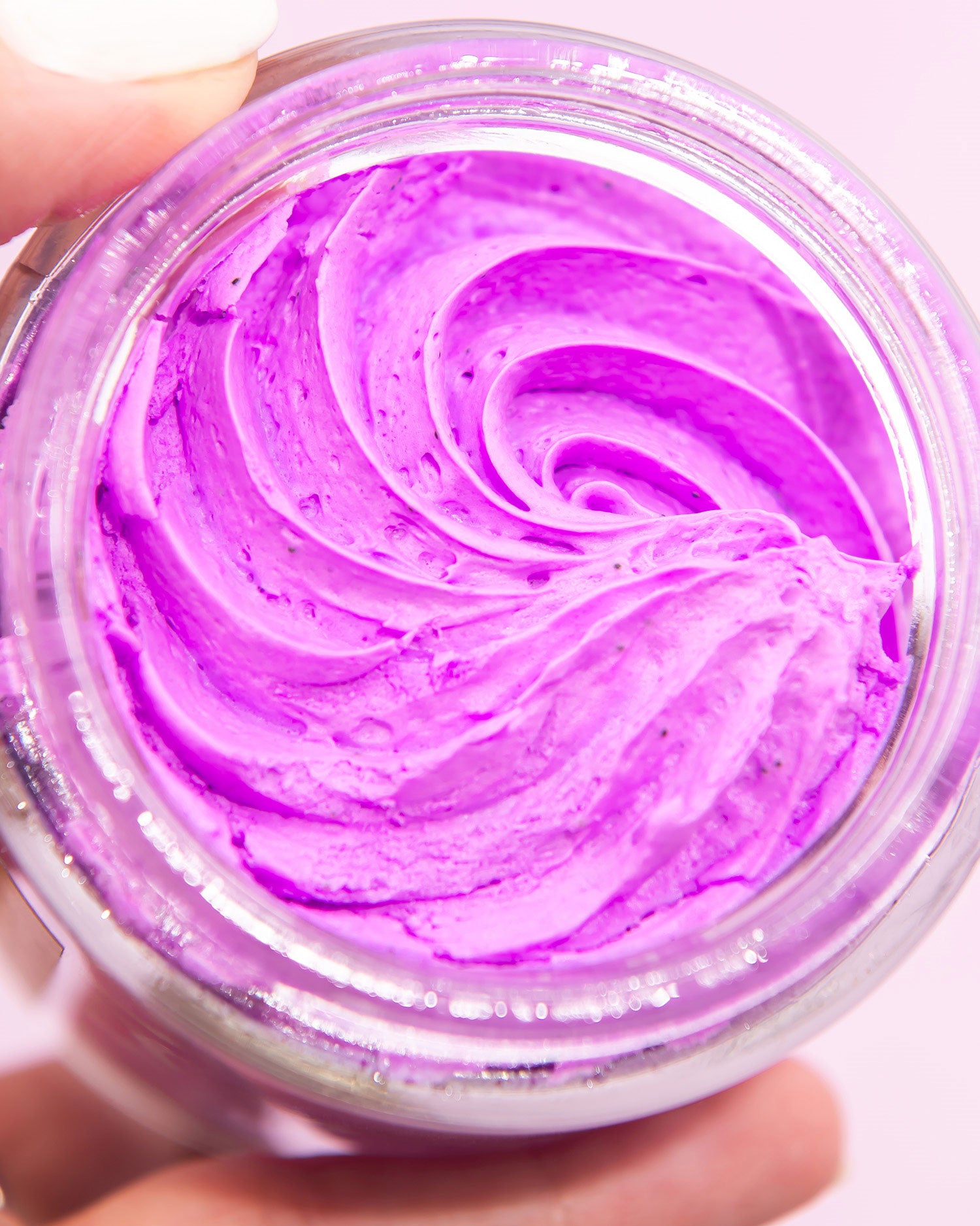 A close-up shows a hand holding a jar of Truly Beautys For Your Boobs Routine, featuring smooth, swirled bright purple cream for boob skincare.