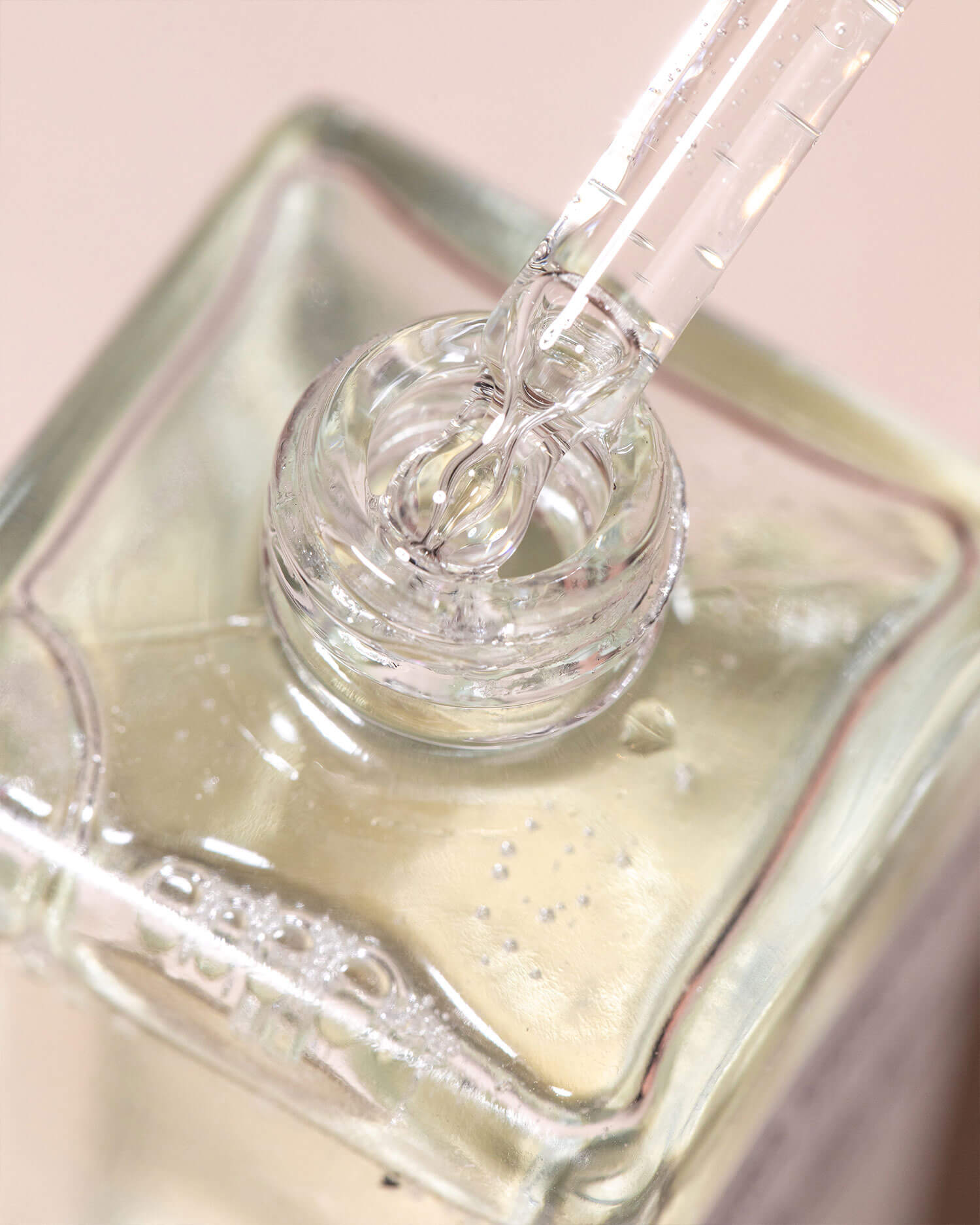 A glass dropper dispenses clear liquid into a square bottle of pale yellow Ultimate Cooka Treatment by Truly Beauty, set against a softly blurred, light background.