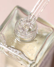 A glass dropper dispenses clear liquid into a square bottle of pale yellow Ultimate Cooka Treatment by Truly Beauty, set against a softly blurred, light background.