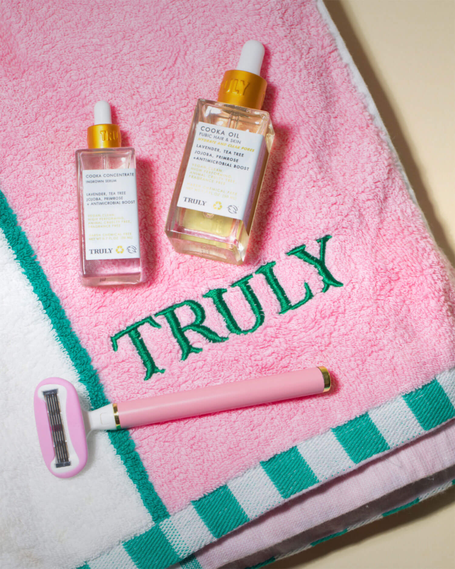 The Truly Beauty Ultimate Cooka Treatment, featuring a pink and white towel with green TRULY embroidery, Cooka Oil serum, and a pink signature razor, is arranged on a light surface.