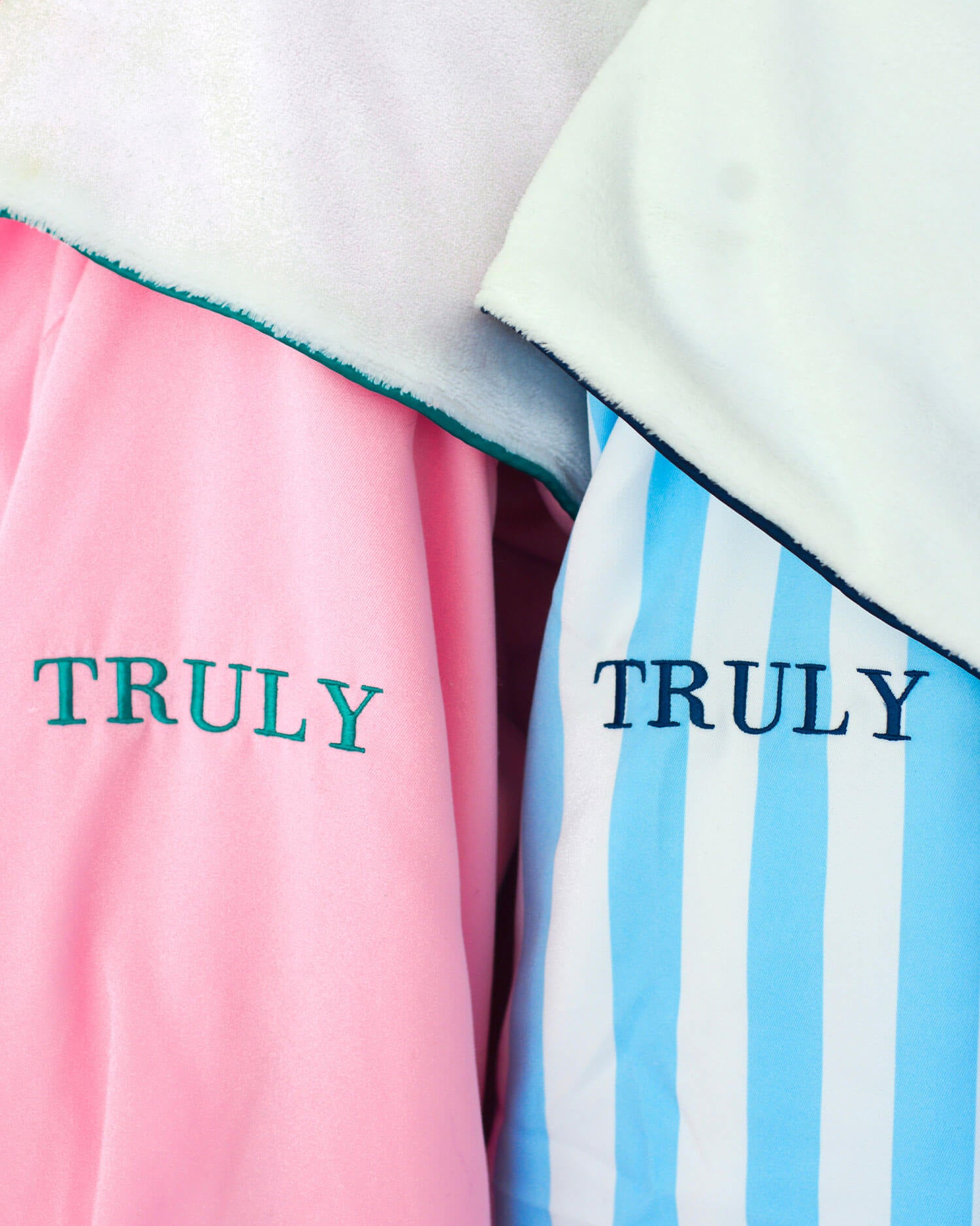 The Mykonos Luxury Robe by Truly Beauty features ultra-soft sherpa lining in both solid pink with green TRULY embroidery and blue-white stripes with navy embroidery, offering extra comfort.