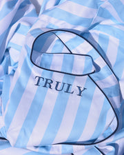A close-up of the Mykonos Luxury Robe by Truly Beauty shows blue and white stripes, dark piping, and the word TRULY embroidered on a pocket. The ultra-soft sherpa lining peeks out, hinting at its cozy warmth.